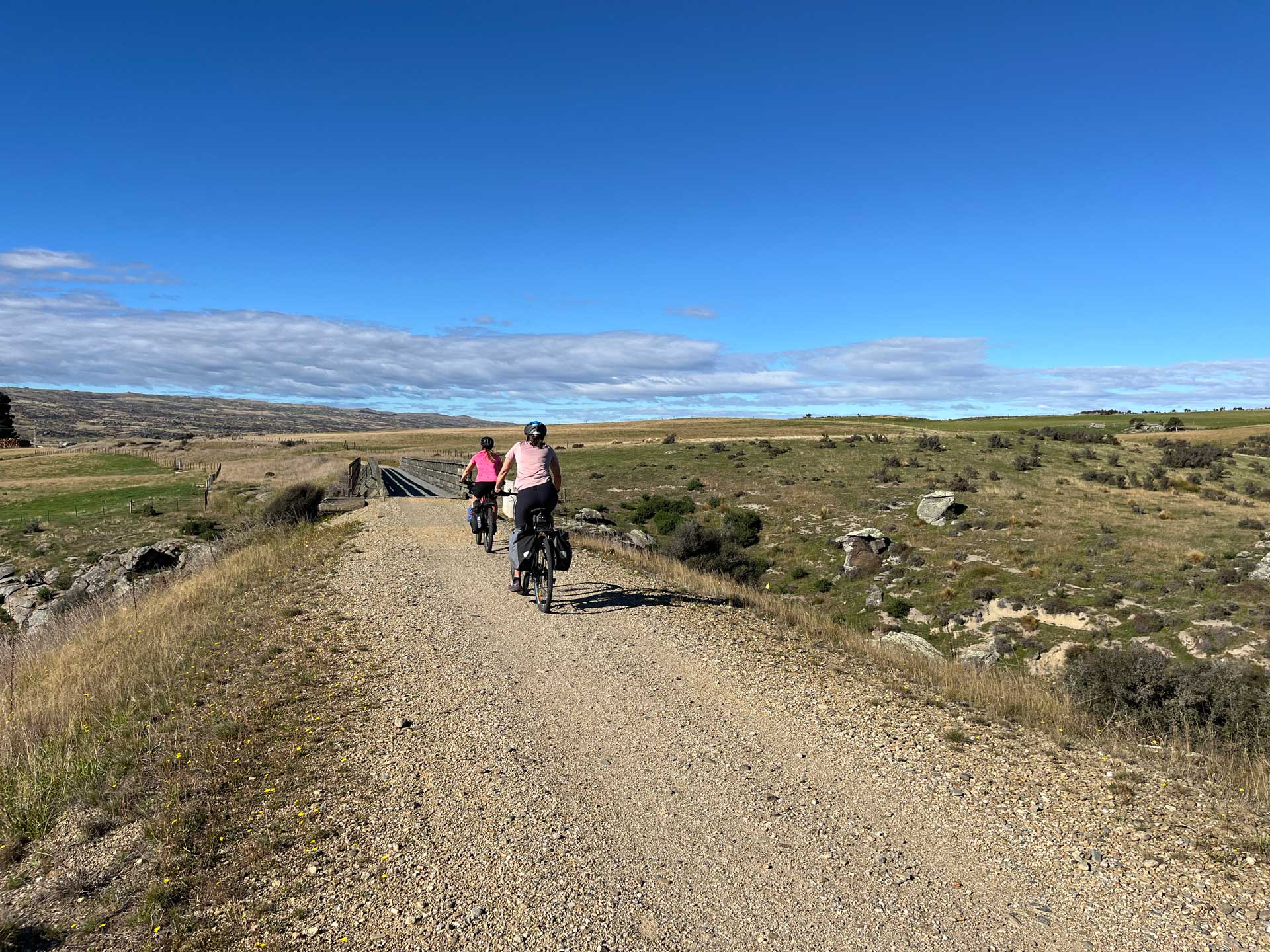 Otago Central Rail Trail, two bikers on gravel track about to cross bridge
